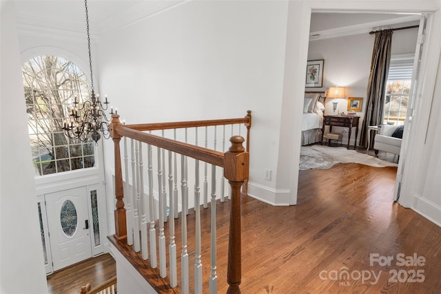 interior space with baseboards, ornamental molding, wood finished floors, an upstairs landing, and a chandelier