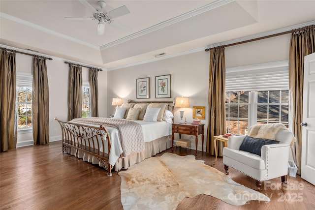 bedroom featuring wood finished floors, visible vents, baseboards, a raised ceiling, and crown molding