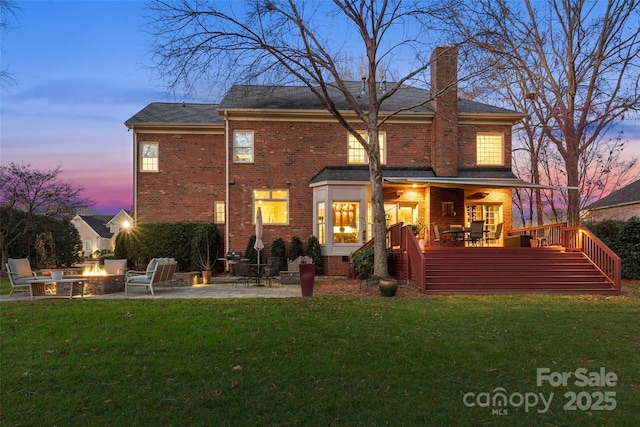 back of house at dusk featuring a fire pit, a patio, a chimney, a wooden deck, and brick siding