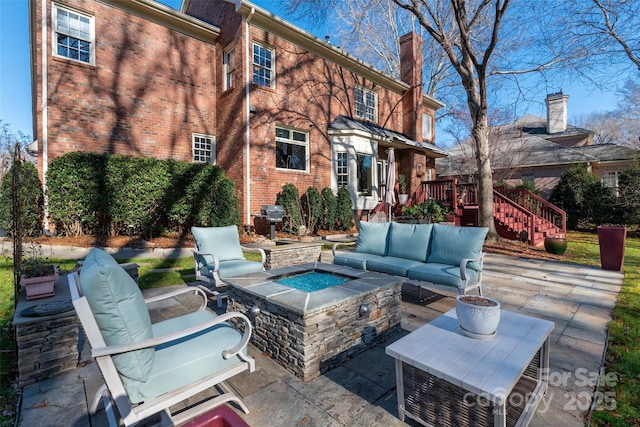 rear view of property with brick siding, stairs, a chimney, a patio area, and an outdoor living space with a fire pit