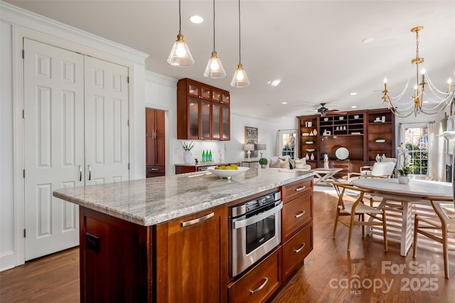 kitchen with hanging light fixtures, glass insert cabinets, open floor plan, a kitchen island, and oven