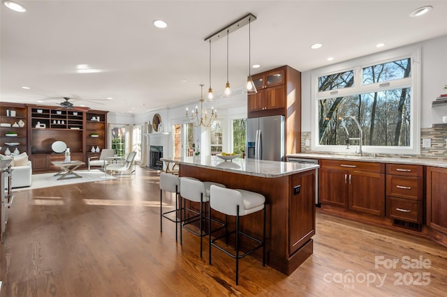 kitchen featuring a breakfast bar area, open floor plan, a center island, a fireplace, and stainless steel refrigerator with ice dispenser