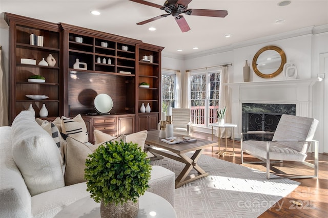 living room featuring a high end fireplace, a ceiling fan, ornamental molding, light wood-style floors, and recessed lighting