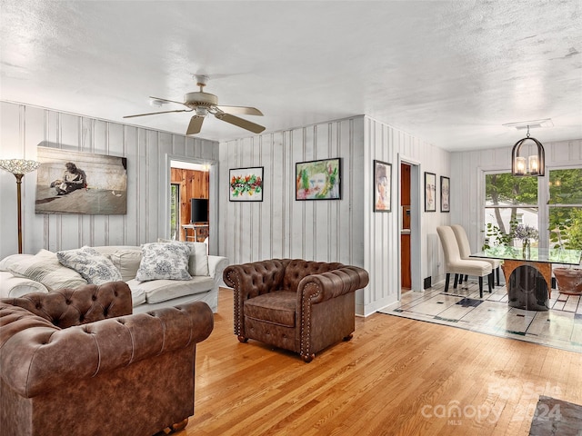 living room featuring ceiling fan with notable chandelier, a textured ceiling, and light wood-type flooring