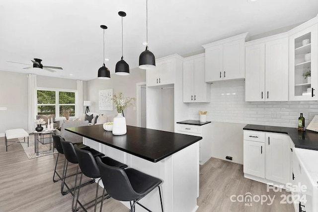 kitchen featuring backsplash, hanging light fixtures, light hardwood / wood-style flooring, ceiling fan, and white cabinetry