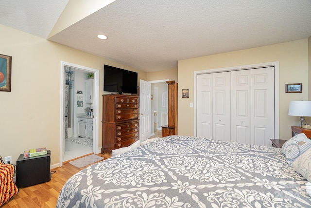 bedroom with connected bathroom, a closet, a textured ceiling, and light wood-type flooring