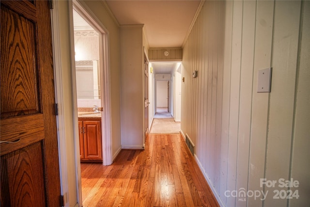 hallway featuring wood walls, sink, light wood-type flooring, and ornamental molding