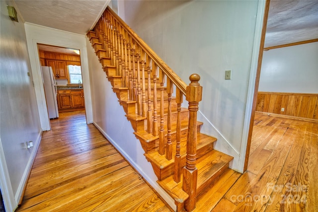 stairs featuring wood walls, wood-type flooring, and ornamental molding