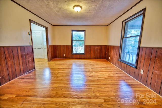 spare room featuring a textured ceiling, light wood-type flooring, ornamental molding, and wooden walls