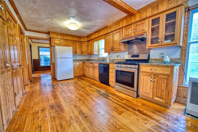 kitchen featuring dishwasher, stainless steel gas stove, white refrigerator, wooden walls, and light wood-type flooring