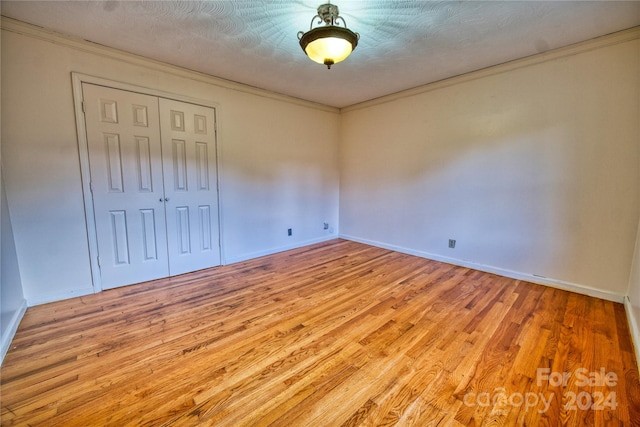 unfurnished bedroom with a textured ceiling, light hardwood / wood-style floors, crown molding, and a closet