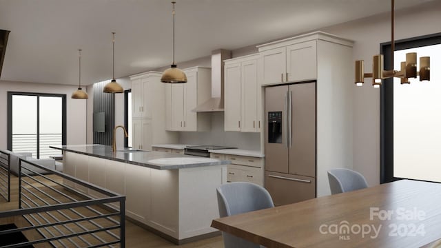 kitchen with stainless steel fridge, a kitchen island with sink, sink, white cabinets, and hanging light fixtures