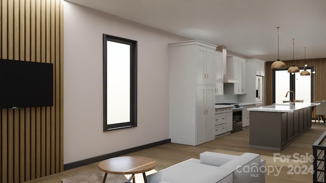 kitchen with stainless steel gas range oven, hanging light fixtures, an island with sink, light hardwood / wood-style floors, and white cabinetry