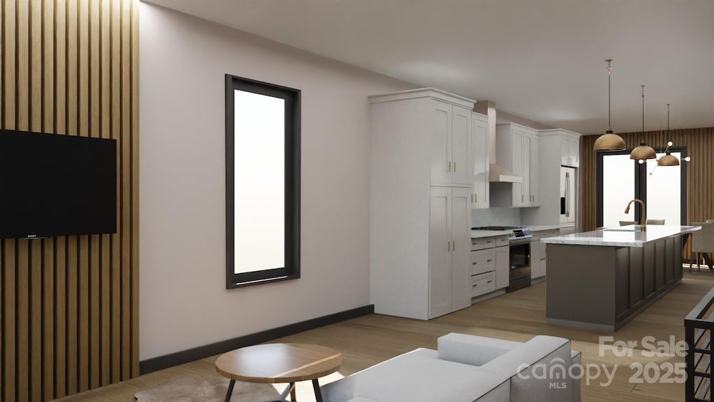 kitchen featuring stainless steel range with gas cooktop, pendant lighting, sink, white cabinets, and a center island with sink