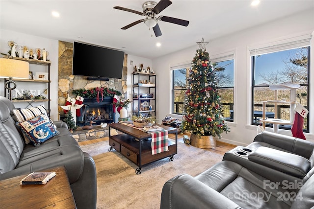 living room featuring light wood-type flooring, a stone fireplace, and ceiling fan