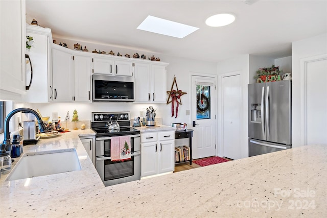 kitchen with a skylight, light stone counters, sink, and stainless steel appliances