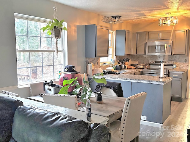 kitchen with decorative light fixtures, a wealth of natural light, appliances with stainless steel finishes, and light hardwood / wood-style flooring