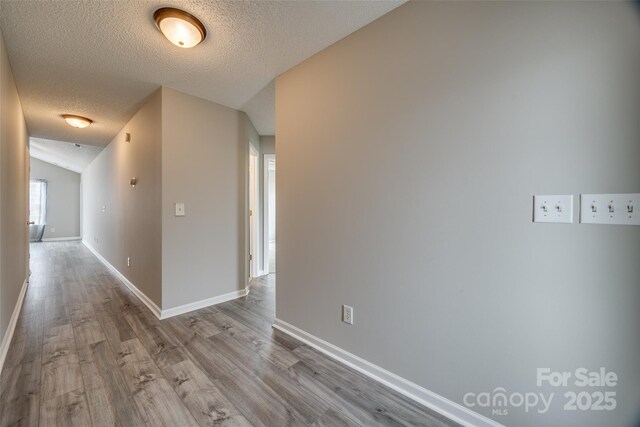 corridor featuring a textured ceiling, light hardwood / wood-style flooring, and vaulted ceiling