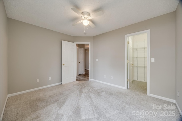 unfurnished bedroom with a walk in closet, ceiling fan, a textured ceiling, light colored carpet, and a closet