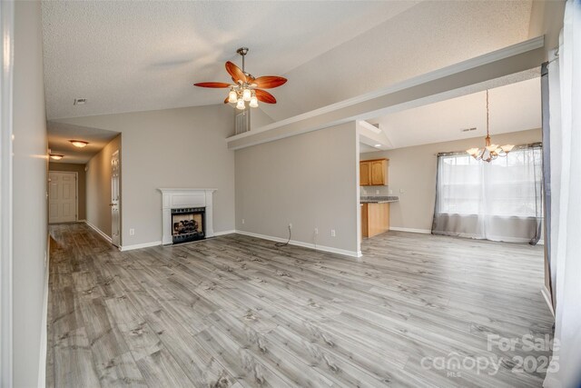 unfurnished living room with ceiling fan with notable chandelier, light hardwood / wood-style floors, a textured ceiling, and vaulted ceiling