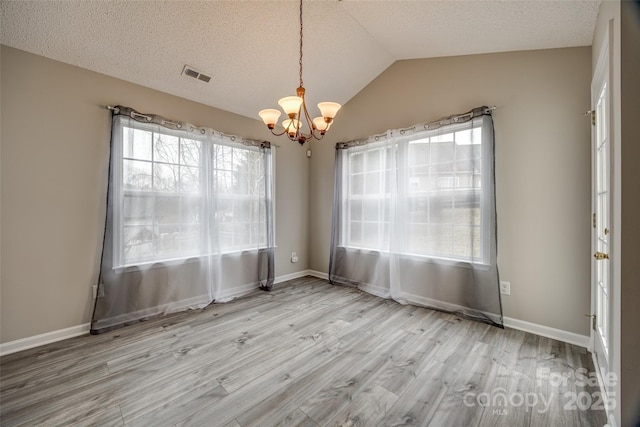 unfurnished dining area featuring light hardwood / wood-style floors, lofted ceiling, a textured ceiling, and a chandelier