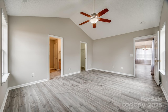 unfurnished bedroom featuring ensuite bathroom, ceiling fan with notable chandelier, a spacious closet, a closet, and lofted ceiling