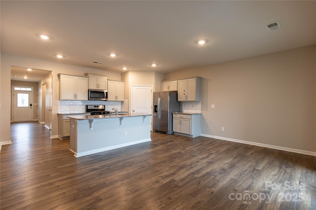 kitchen featuring appliances with stainless steel finishes, a kitchen breakfast bar, dark hardwood / wood-style flooring, an island with sink, and decorative backsplash