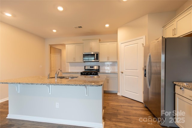 kitchen featuring a kitchen bar, sink, a center island with sink, appliances with stainless steel finishes, and dark hardwood / wood-style floors