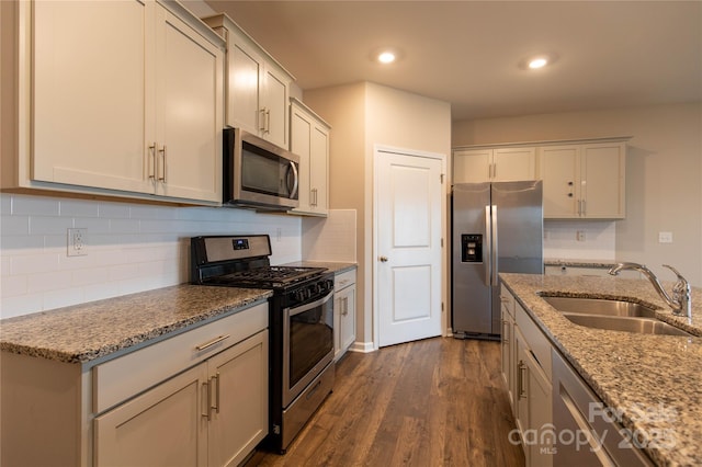 kitchen featuring sink, dark wood-type flooring, backsplash, stainless steel appliances, and light stone counters