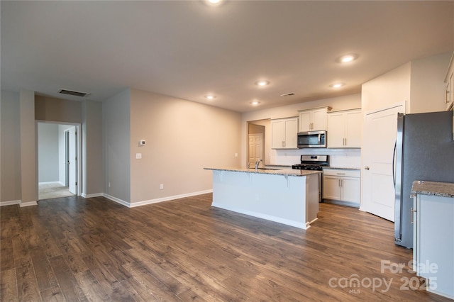 kitchen featuring appliances with stainless steel finishes, white cabinetry, an island with sink, light stone counters, and dark wood-type flooring