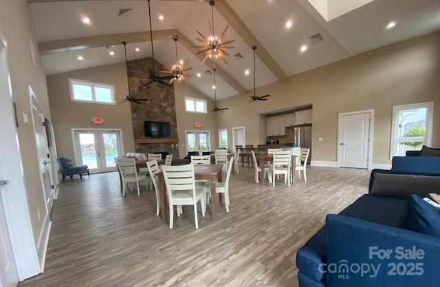 dining area featuring ceiling fan, hardwood / wood-style floors, a towering ceiling, a stone fireplace, and french doors