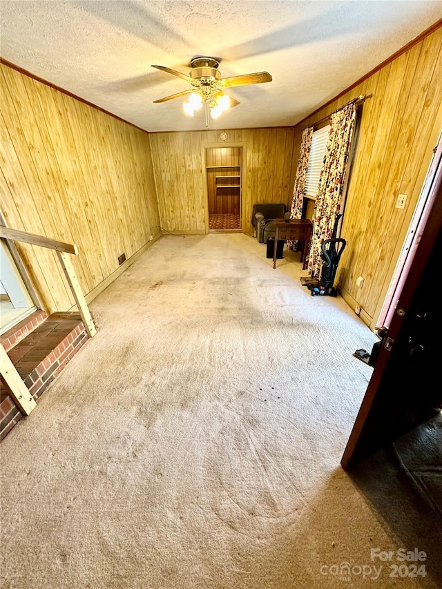 interior space featuring carpet, ceiling fan, a textured ceiling, and wooden walls