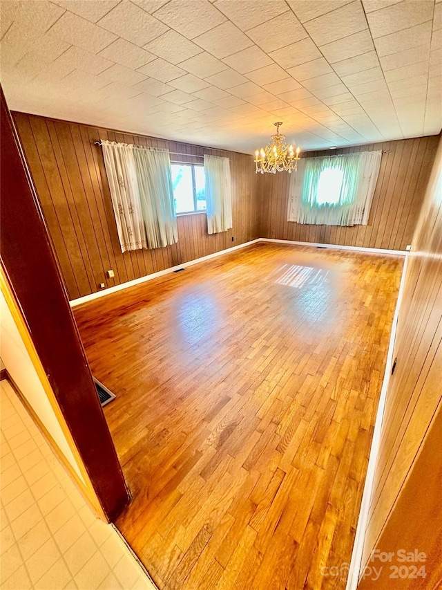 unfurnished room featuring wood walls, an inviting chandelier, and hardwood / wood-style flooring