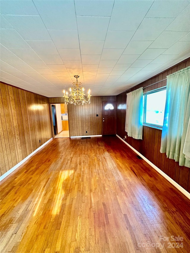 unfurnished room featuring wood walls, hardwood / wood-style floors, and an inviting chandelier