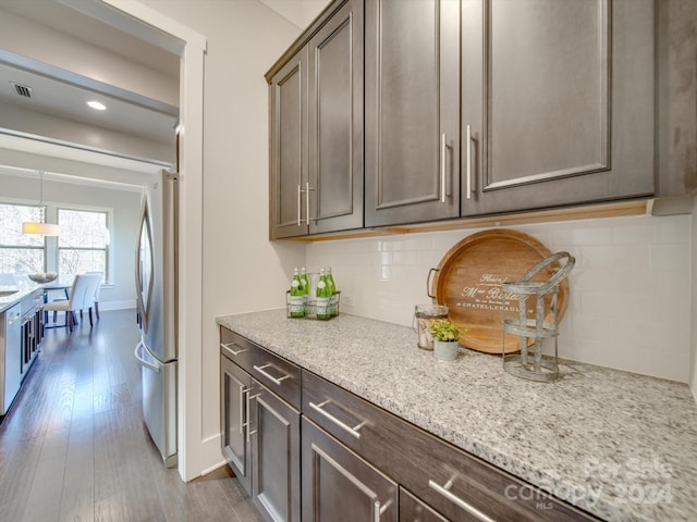 kitchen with decorative backsplash, light stone countertops, dark brown cabinets, light hardwood / wood-style floors, and stainless steel appliances