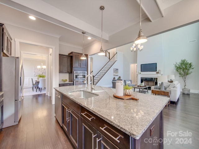 kitchen with appliances with stainless steel finishes, dark hardwood / wood-style flooring, dark brown cabinetry, a kitchen island with sink, and pendant lighting