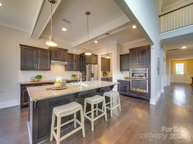 kitchen featuring pendant lighting, dark hardwood / wood-style floors, light stone countertops, an island with sink, and appliances with stainless steel finishes