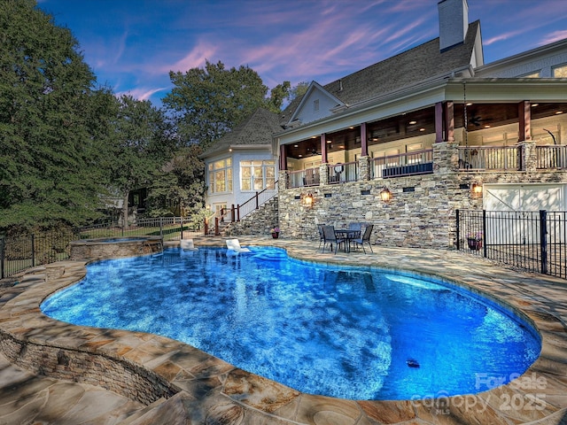 pool at dusk featuring ceiling fan and a patio