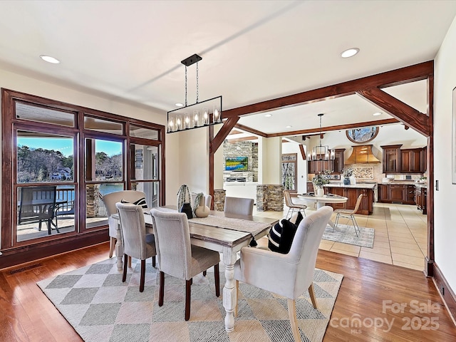 dining room with beam ceiling, light hardwood / wood-style floors, a notable chandelier, and a water view