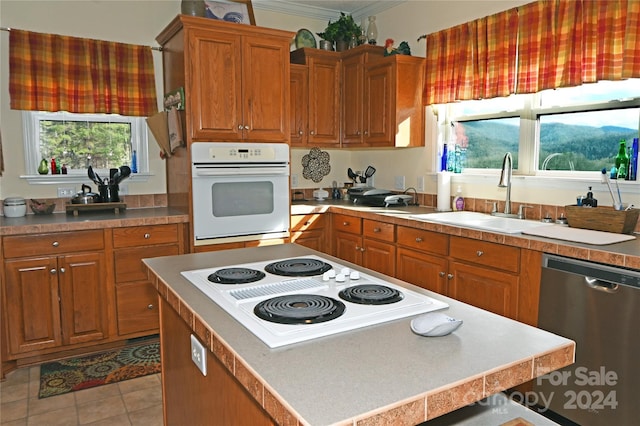 kitchen with sink, a center island, crown molding, white appliances, and light tile patterned floors