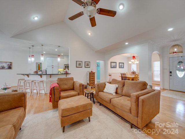 living room with ceiling fan with notable chandelier, light wood-type flooring, and high vaulted ceiling