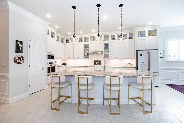 kitchen with a center island with sink, light stone countertops, ornamental molding, and appliances with stainless steel finishes