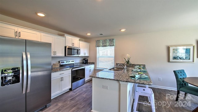 kitchen featuring appliances with stainless steel finishes, dark hardwood / wood-style flooring, dark stone counters, sink, and white cabinetry