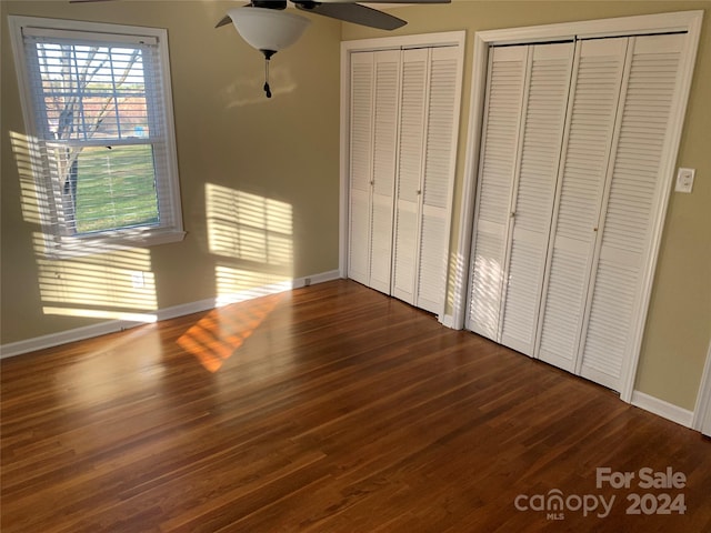 unfurnished bedroom with dark hardwood / wood-style floors, ceiling fan, and two closets