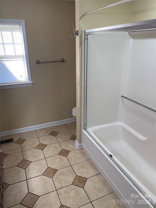 bathroom featuring tile patterned flooring, toilet, and shower / bath combination with glass door