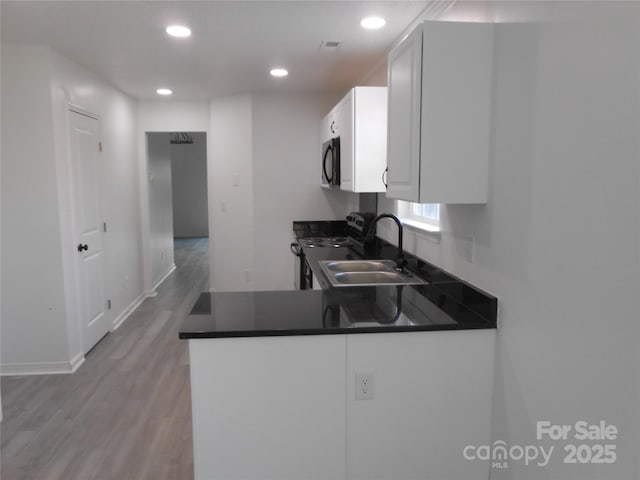 kitchen with dark countertops, electric range oven, a sink, black microwave, and a peninsula