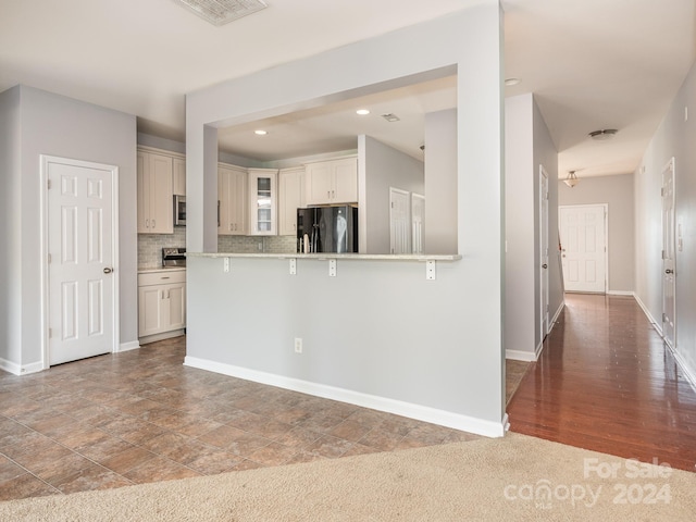 kitchen featuring carpet flooring, white cabinetry, tasteful backsplash, black fridge, and kitchen peninsula