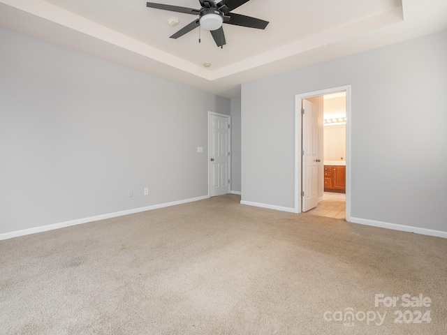 unfurnished bedroom with a raised ceiling, ceiling fan, ensuite bathroom, and light carpet