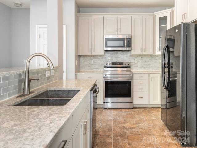 kitchen featuring backsplash, light stone counters, sink, and appliances with stainless steel finishes