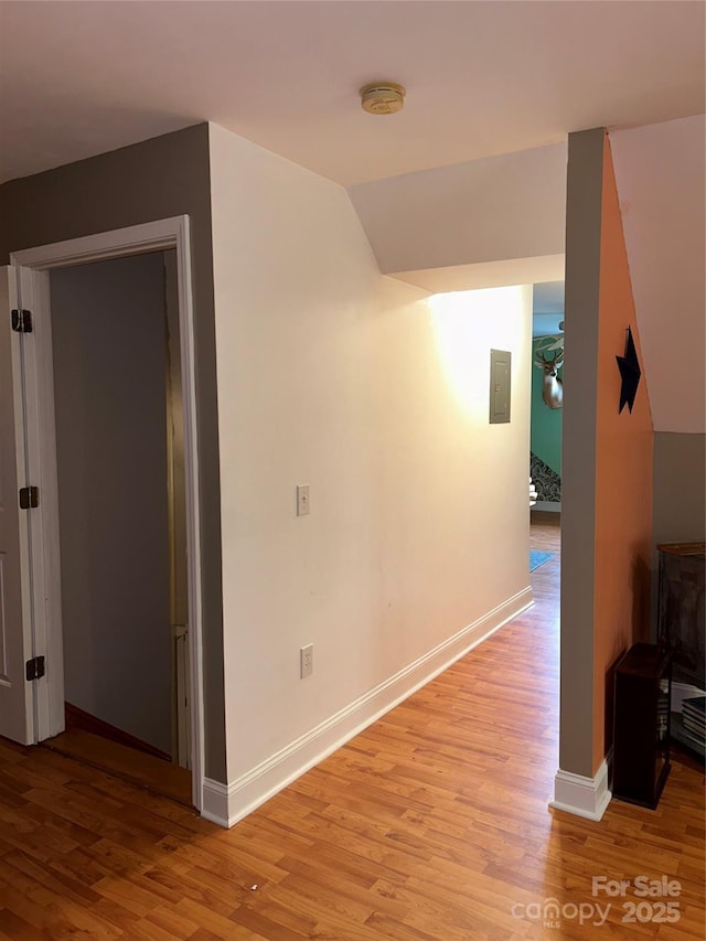 hallway featuring light hardwood / wood-style floors, electric panel, and vaulted ceiling